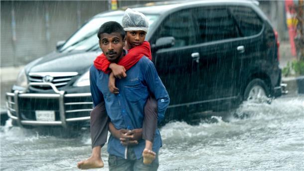 Ein Mann trägt in Dhaka einen Jungen auf dem Rücken, während er auf einer überschwemmten Straße geht.