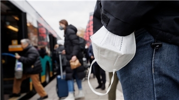 Ein Mann wartet mit einer Maske am Handgelenk auf einen Bus.