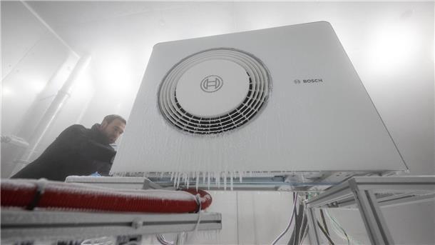 Ein Mitarbeiter der Bosch Thermotechnik GmbH öffnet in einer Klimakammer das Gehäuse einer Bosch-Wärmepumpe.