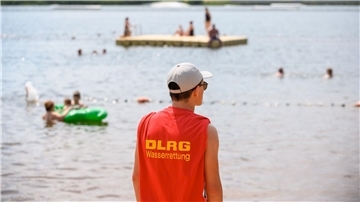 Ein Mitglied der Deutschen Lebens-Rettungs-Gesellschaft (DLRG) steht in einem Strandbad am Ufer.