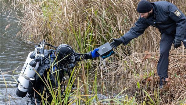 Nach Golddiebstahl: Spurensuche und Debatte um Kameraanlage Ein Polizeitaucher reicht einen gefundenen Gegenstand an einen Kollegen weiter, der er zuvor aus dem Pichler Weiher in der Nähe des Keltenmuseums gefunden hat.