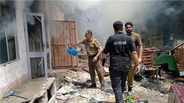 Wütende Menschenmenge in Pakistan greift Kirchen an Ein Polizist kippt der Wasser aus einem Gefäß in ein brennendes Gebäude.