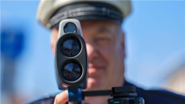 Ein Polizist misst mit einem Laserhandmessgerät (Laserpistole) während einer Geschwindigkeitskontrolle einen Autofahrer.
