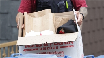 Ein Polizist trägt nach einer Wohnungsdurchsuchung einen Karton mit sichergestellten Gegenständen.