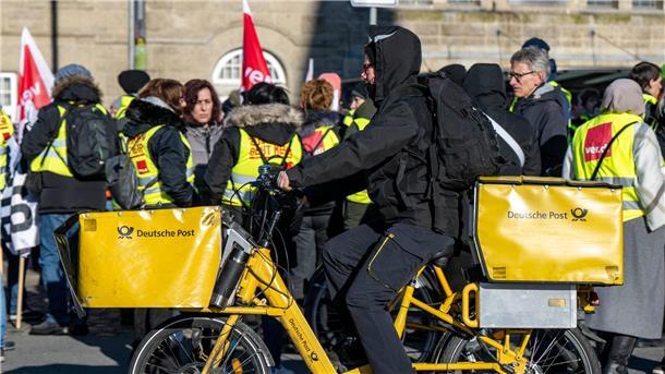 Sorgen trotz Rekordzahlen: Post-Tarifkonflikt schwelt weiter Ein Postbote radelt in Bielefeld an Streikenden einer Verdi-Aktion vorbei.