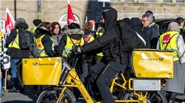 Ein Postbote radelt in Bielefeld an Streikenden einer Verdi-Aktion vorbei.
