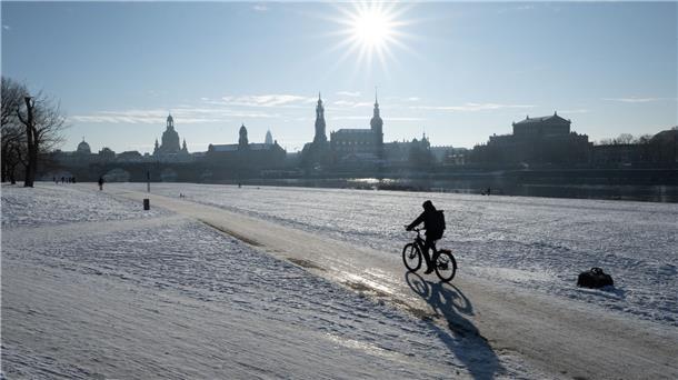 Ein Radfahrer fährt am Ufer der vor der Kulisse der Altstadt von Dresden durch den Schnee.