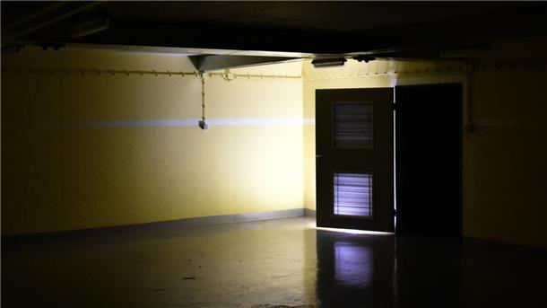 Ein dunkler Raum in einem Bunker. Am Ende des Raumes ist eine Tür geöffnet, Licht scheint herein.