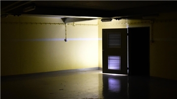 Ein dunkler Raum in einem Bunker. Am Ende des Raumes ist eine Tür geöffnet, Licht scheint herein.