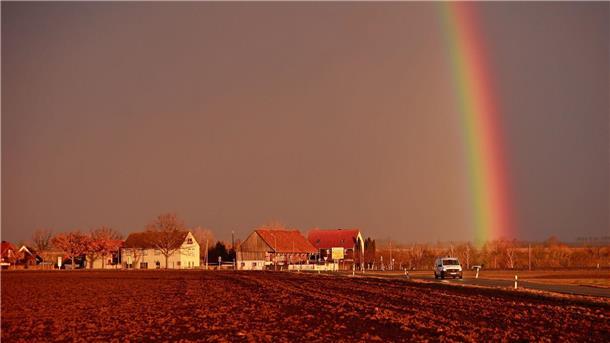 Sturm und Regen sorgen für Beeinträchtigungen Ein Sturmtief kündigt sich bei tief stehender Sonne mit starkem Wind an, während sich ein Regenbogen am Himmel gebildet hat.