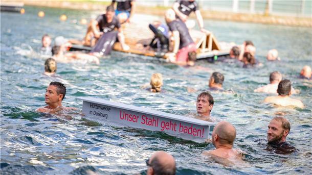 Ein symbolischer Stahlträger mit dem Slogan der Demo schwimmt im Duisburger Innenhafen zwischen zahlreichen Stahlbeschäftigten.