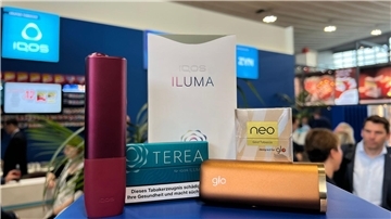 Ein Tabakerhitzer der Marke Iqos vom Hersteller Philip Morris und ein dazugehöriges Päckchen Tabaksticks der Marke Terea sowie das Konkurrenzprodukt Glo (mit Neo-Tabaksticks) des Herstellers BAT liegen bei der Fachmesse Intertabac in einer Messehalle.