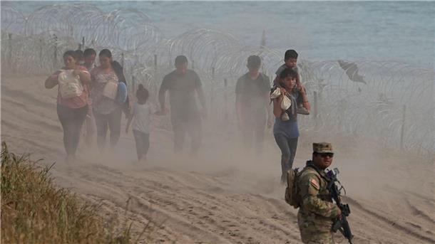 Ein texanischer Wachmann neben Menschen, die den Rio Grande von Mexiko aus in die USA überquert haben.