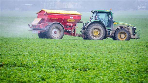 Bundestag beschließt Änderungen am Düngegesetz Ein Traktor fährt mit einem Streuwagen über ein Feld und bringt Dünger aus.