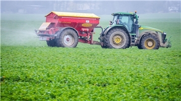 Ein Traktor fährt mit einem Streuwagen über ein Feld und bringt Dünger aus.