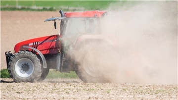 Ein Traktor fährt über einen staubtrockenen Acker.