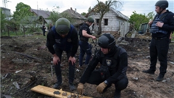 Ein ukrainischer Polizeibeamter und ein Staatsanwalt für Kriegsverbrechen inspizieren Bruchstücke einer Gleitbombe vor einem beschädigten Haus nach einem russischen Luftangriff auf ein Wohnviertel.