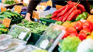 Ein Verkäufer greift an einem Obst- und Gemüsestand auf dem Wochenmarkt in eine Kiste mit Erbsen.