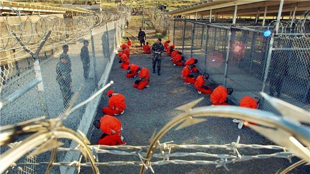 Ein von der US-Armee herausgegebenes Foto aus dem Jahr 2002 zeigt in orangefarbene Overalls gekleidete Häftlinge, die im Camp X-Ray auf dem Boden knien.