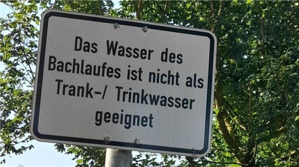 Ein Schild auf dem steht: "Das Wasser des Bachlaufes ist nicht als Trank-/Trinkwasser geeignet"