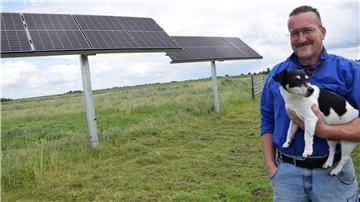Mann mit Hund vor zwei Solarmodulen.