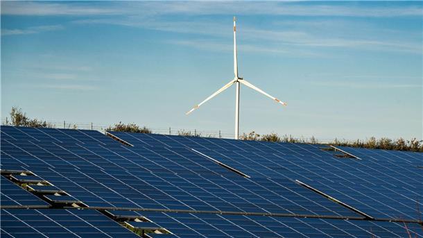 Ein Windrad steht auf einem Hügel einer großflächigen Solaranlage.