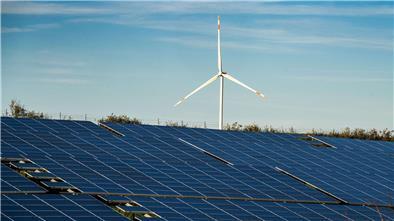 Ein Windrad steht auf einem Hügel einer großflächigen Solaranlage.