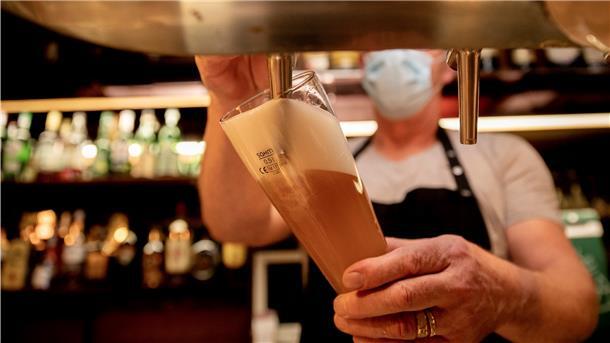Ein Wirt mit Maske zapft in einer Kneipe Bier. Bei hohen Infektionszahlen dürfen Kommunen und Landkreise für die Gastronomie Sperrstunden verhängen. Aber nur wenige Landkreise machen bislang davon Gebrauch.