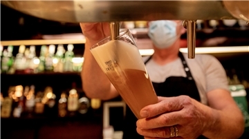 Ein Wirt mit Maske zapft in einer Kneipe Bier. Bei hohen Infektionszahlen dürfen Kommunen und Landkreise für die Gastronomie Sperrstunden verhängen. Aber nur wenige Landkreise machen bislang davon Gebrauch.