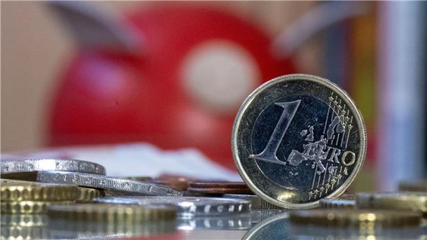Eine 1-Euro-Münze steht vor einem Sparschwein. 