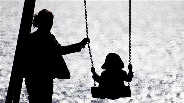 Eine alleinerziehende Mutter schaukelt ihr Kind auf einem Spielplatz.