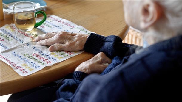 Eine demenzkranke Frau sitzt an eeinem Tisch.