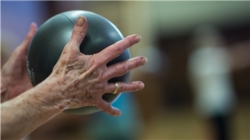 Eine Frau macht in der Seniorengymnastik eine Übung mit dem Ball.