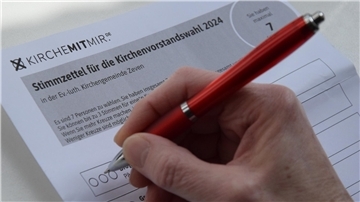 Eine Frau setzt ein Kreuz auf einen Stimmzettel für die Wahl des Kirchenvorstands in Zeven.