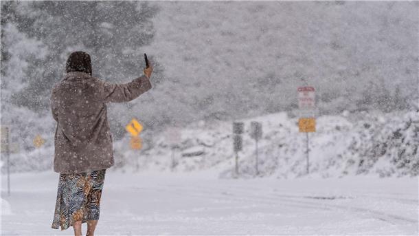 Wintersturm fegt über die USA - Ein Feuerwehrmann tot Eine Frau steht auf einer schneebedeckten Straße und macht ein Selfie im Angeles National Forest.