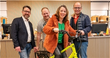 Eine Frau sitzt auf einem gelben Lastenrad. Drei Männer stehen drumherum.