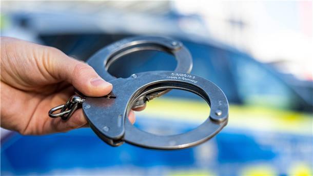 Schusswaffeneinsatz: Festnahme von mutmaßlichem Einbrecher Eine Hand hält Handschellen vor einen Streifenwagen der Polizei.
