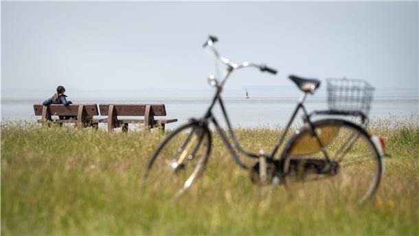 Eine Radfahrerin sitzt auf einer Bank am Deich.