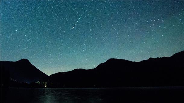 Eine Sternschnuppe leuchtet neben der Milchstraße am Himmel über dem Walchensee.