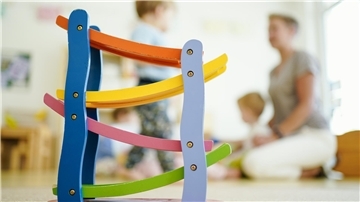 Eine Erzieherin spielt in einer Kindertagesstätte hinter einer Rollbahn mit Kindern.Eine Studie zeigt: Viele Erzieherinnen und Erzieher verlassen den Beruf früh oder reduzieren ihre Stunden. Nur ein Drittel bleibt auch nach zehn Jahren in der Kindertagesbetreuung im Land Bremen tätig.
