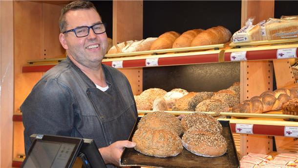 Matthias Jantzen hält ein Backblech in seinen Händen. Darauf befinden sich vier Brote. 