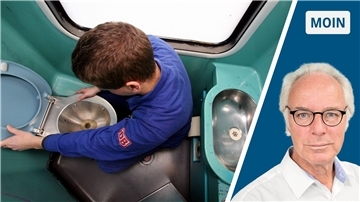 Ein Mitarbeiter der Deutschen Bahn beugt sich über eine Zugtoilette.