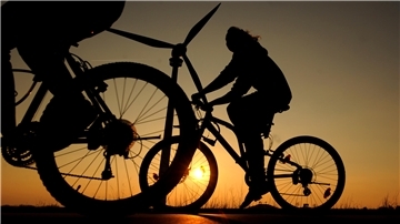 Fahrradfahrer vor der untergehenden Sonne und einem Windkraftrad.