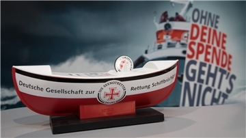 Ein Bootsmodell der Deutschen Gesellschaft zur Rettung Schiffbrüchiger steht vor einem Plakat mit der Aufschrift "Ohne deine Spende geht's nicht".