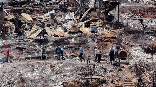 Zahl der Toten bei Waldbränden in Chile steigt auf 112 Einheimische arbeiten zwischen den Trümmern von ausgebrannten Häusern.