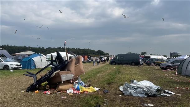 Nach der Party ist vor dem Aufräumen: Müll auf Deichbrand-Gelände Sofas und Plastikmöbel auf einem Haufen auf einer Wiese. Drumherum Zelte und Autos. Am Himmel kreisen Möwen.
