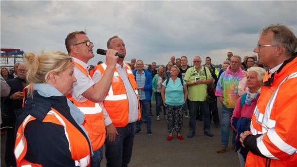 Menschen stehen in einer Menge zusammen. Ein Mann spricht in ein Mikrofon.
