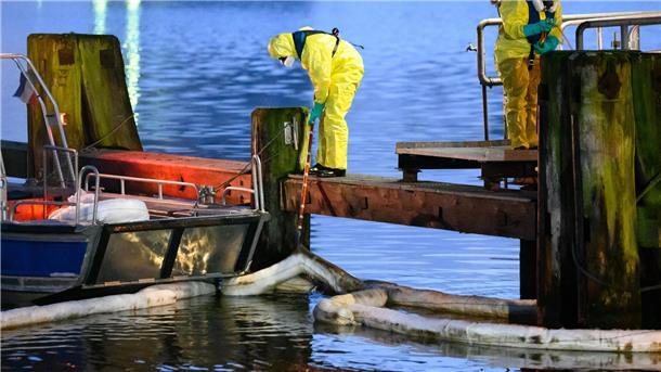 Einsatzkräfte des THW in Schutzanzügen arbeiten mit Ölschlengeln an einem Steg. Aus einem Leck in einer Pipeline im Hafen von Brunsbüttel sind große Mengen Öl in den Nord-Ostsee-Kanal gelaufen.