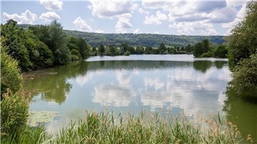 Einzelne Wolken ziehen über einen Badesee hinweg.