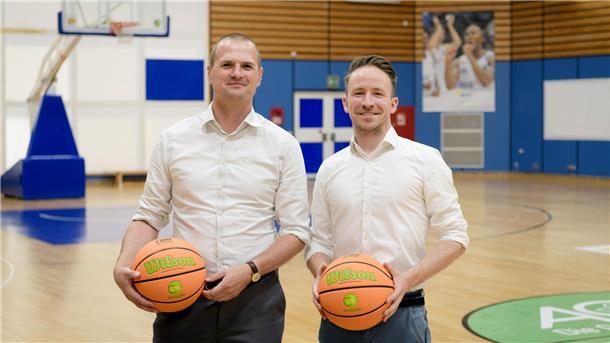 Zwei Männer stehen nebeneinander und halten einen Basketball in den Händen.